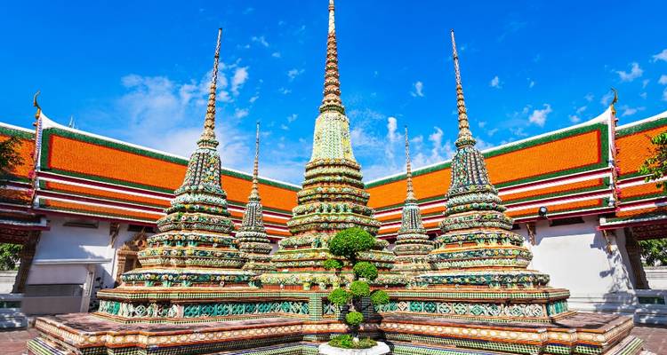 Stupas coloridas y agujas ornamentadas de Wat Pho bajo un cielo azul vibrante.