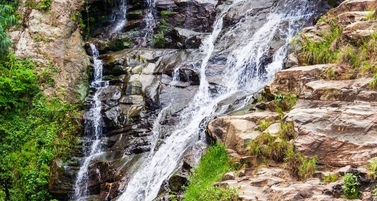 Wiederholte Nahaufnahme eines kaskadierenden Wasserfalls über rauen Felsen, umgeben von Vegetation
