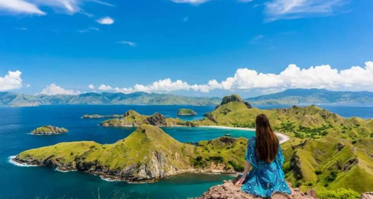 Frau sitzt auf felsigem Gipfel mit Blick auf dramatische smaragdgrüne Inseln und tiefblaues Meer unter klarem Himmel