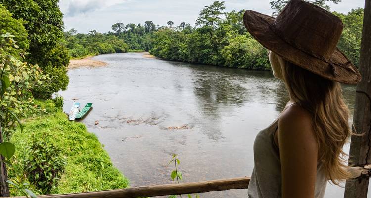 Persona contemplando un río rodeado de espeso bosque.
