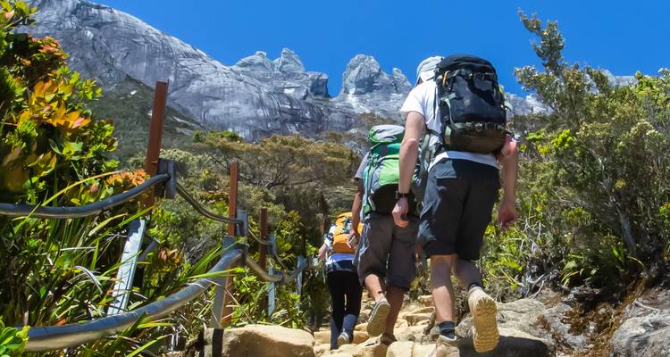 Excursionistas caminando por un sendero rocoso con montañas de fondo.