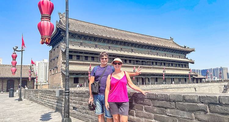 Dos turistas posando en la muralla de la ciudad de Xi'an con decoraciones de linternas rojas.