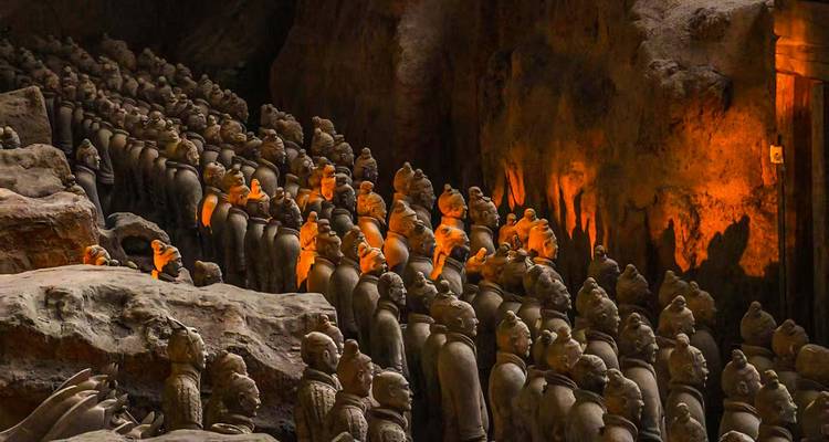 Filas de Guerreros de Terracota se mantienen en silencio en fosos de tierra iluminados por cálida iluminación interior.