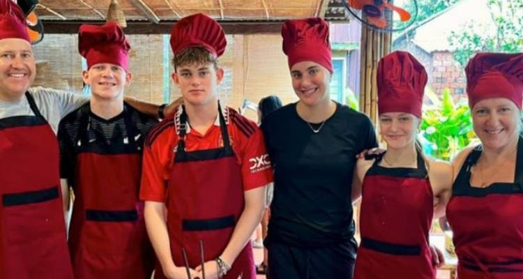 Groupe portant des chapeaux de chef et des tabliers assortis posant pendant un cours de cuisine vietnamienne.