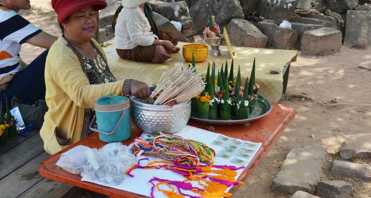 Market vendor displays handmade bracelets, incense and offerings on a low table in an outdoor stall.