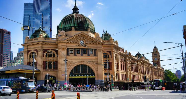La façade jaune ornementée et le dôme vert de la gare de Flinders Street dominent un carrefour animé de Melbourne avec des tramways et des piétons.