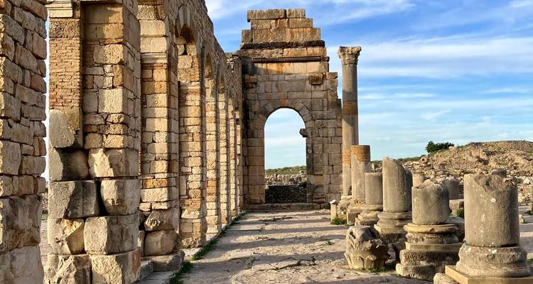 Sonnenbeschienene Säulen und Bögen der antiken römischen Ruinen von Volubilis unter blauem Himmel.