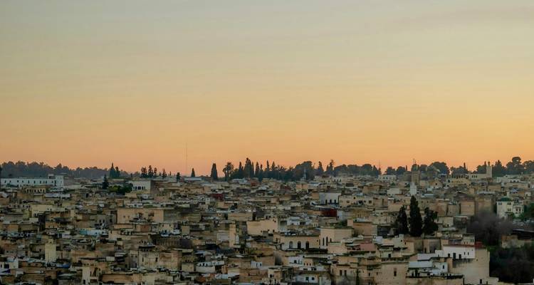 Weite Aussicht auf die Dächer der Medina von Fes bei Sonnenuntergang mit einem orangefarbenen Dämmerungshimmel.