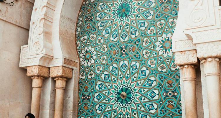 Komplizierter türkisfarbener Mosaikbrunnen und Bögen der Hassan-II-Moschee mit einem Besucher in der Nähe.