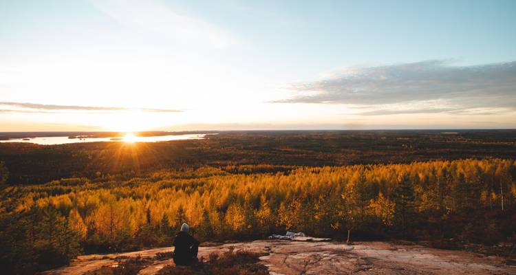 Malerischer Sonnenuntergangsblick mit einer Person, die auf einem Hügel sitzt.