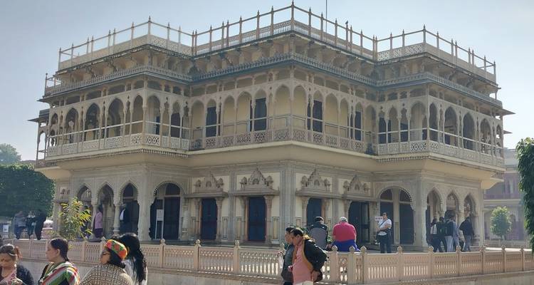 Ornate sandstone palace building with arched balconies inside an Indian complex under hazy sky.