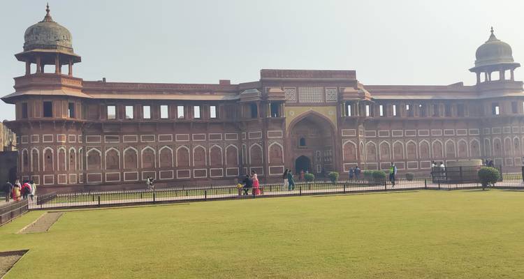 Long rectangular Agra Fort building with lawn foreground under hazy bright sky.