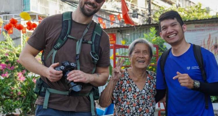 Les voyageurs rient et posent avec une femme âgée locale dans un quartier dynamique orné de drapeaux et de fleurs.