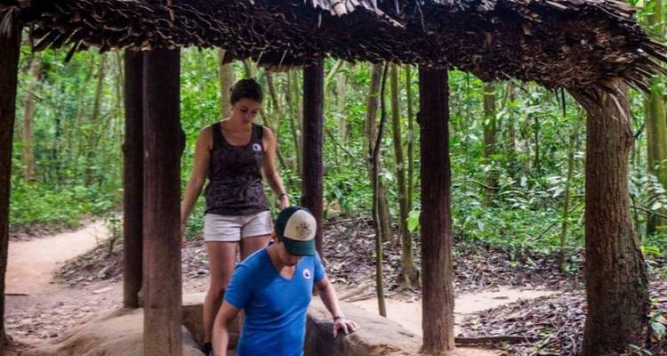 Les voyageurs émergent d'une entrée de tunnel étroite dans une zone forestière du site des Tunnels de Cu Chi.