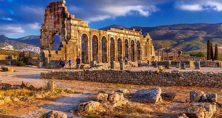 Ancient ruins with stone arches against a mountainous backdrop.