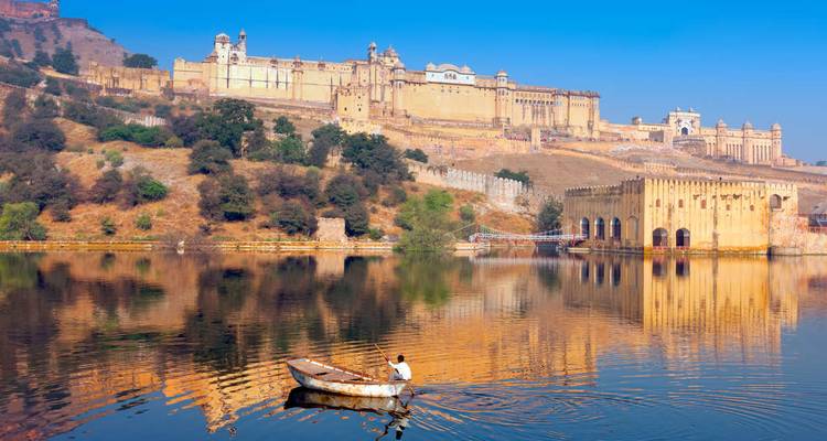Ein malerischer Blick auf das Amber Fort mit einer Person, die ein Boot auf dem See in Jaipur, Indien rudert.