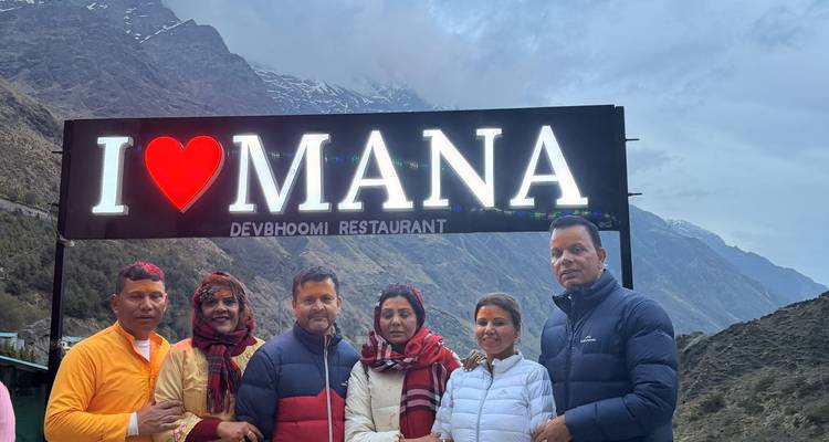 Reisende stehen unter einem beleuchteten "I ♥ MANA"-Schild vor schneebedeckten Himalaya-Gipfeln in der Abenddaemmerung.