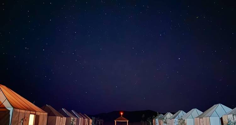Ciel étoilé au-dessus d'un campement dans le désert avec des rangées de tentes.