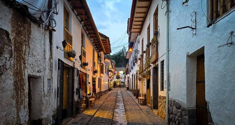 Ruelle étroite pavée de galets flanquée de maisons coloniales blanchies à la chaux dans le quartier historique de Cusco au crépuscule.