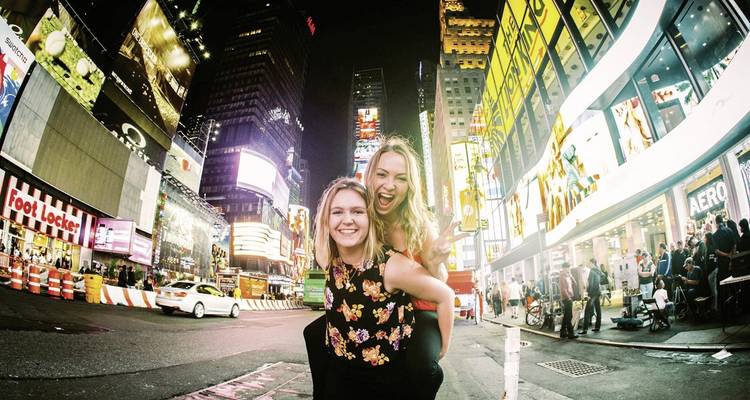 Two people posing in Times Square with vivid neon lights at night.