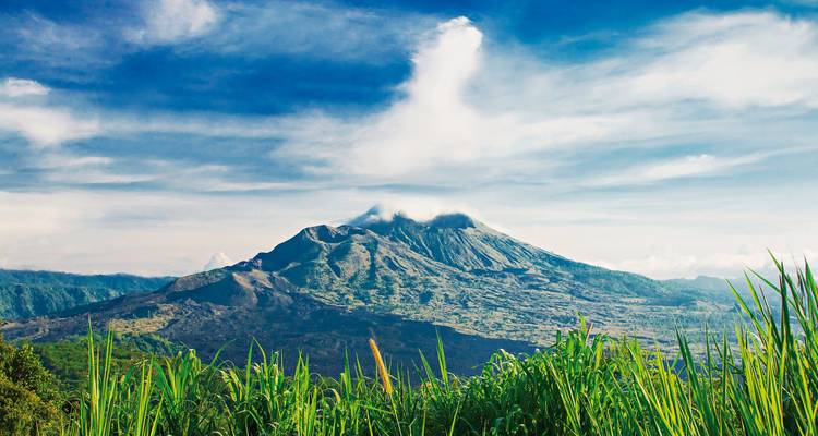 Une montagne volcanique avec une légère couverture nuageuse et de la verdure au premier plan.