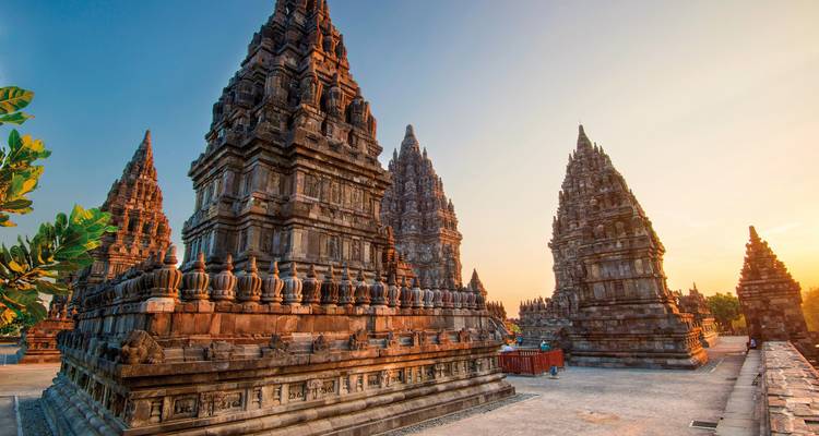Complexe du temple de Prambanan avec des sculptures sur pierre complexes sous un ciel de coucher de soleil.
