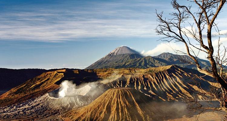 Rauchender Krater und geschichtete Vulkankämme des Mount Bromo mit dem Mount Semeru in der Ferne unter klarem Himmel.