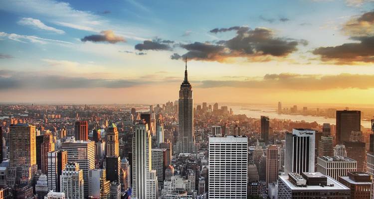 New York City skyline bij zonsondergang met het Empire State Building badend in warm licht.