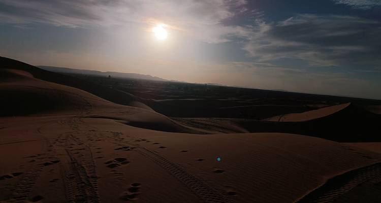 Dunes de sable au crépuscule avec des traces de pneus et un soleil couchant.
