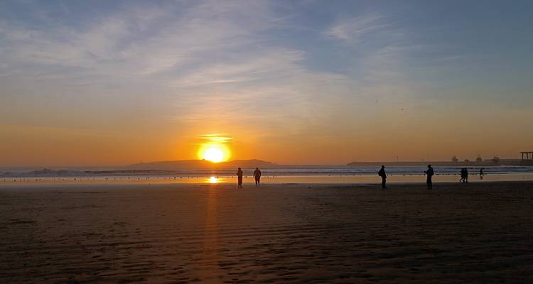 Plage au coucher du soleil avec des silhouettes de personnes qui marchent.
