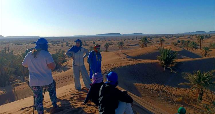 Des gens debout sur des dunes de sable avec des palmiers éparpillés.