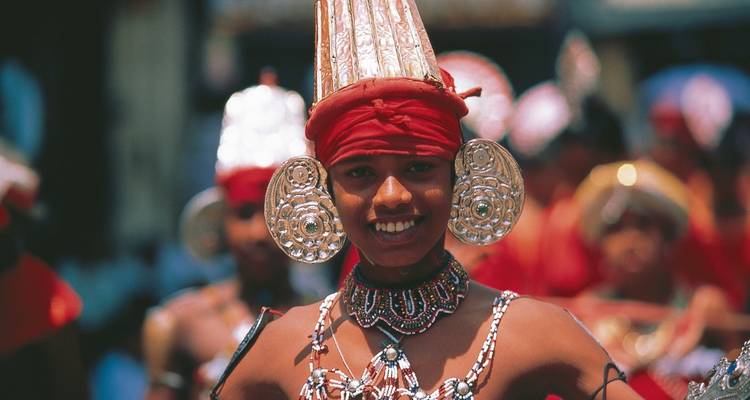Lächelnder sri-lankischer Performer in aufwendigem traditionellem Kostüm und Kopfschmuck während eines Festivals.