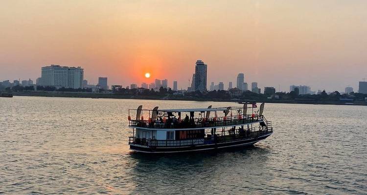 Sonnenuntergangsblick auf ein Boot auf einem Fluss mit einer Stadtsilhouette im Hintergrund.