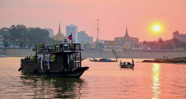 Ein Boot bei Sonnenuntergang mit Blick auf traditionelle Architektur und Stadtsilhouette am Flussufer.