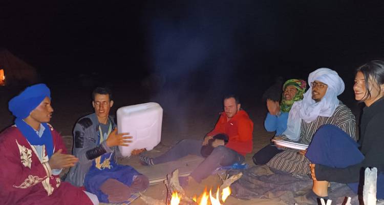 Groupe de personnes se rassemblant autour d'un feu de camp dans le désert la nuit.