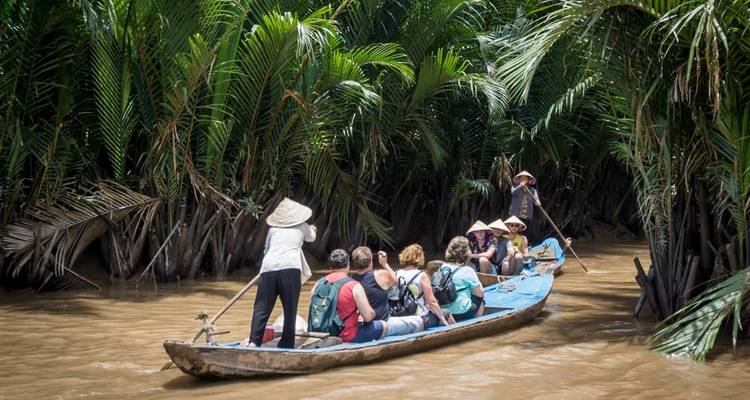 Menschen auf einem Holzboot fahren durch einen üppig grünen Fluss.