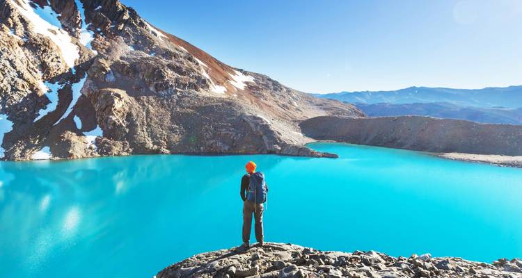 Person, die über einen leuchtend blauen See in einer Bergregion blickt.