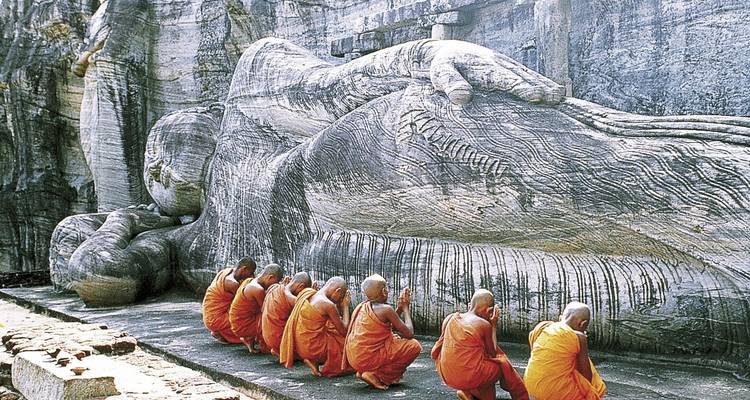 Mönche, die vor einer großen liegenden Buddha-Statue beten.