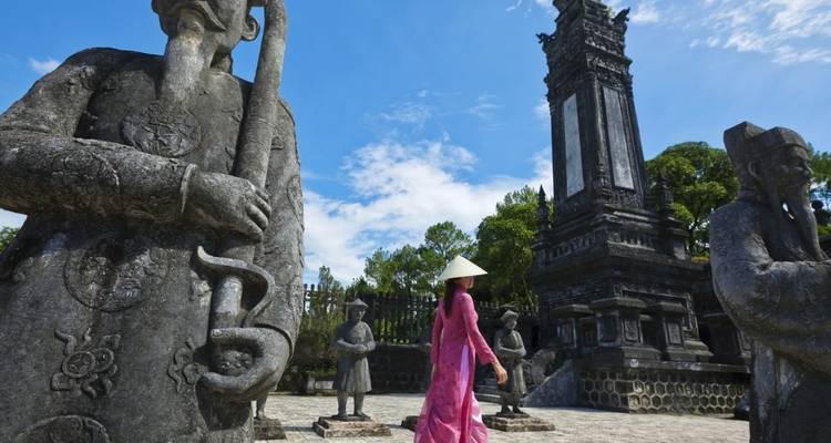Woman in traditional clothing walking among statues in a historical site.
