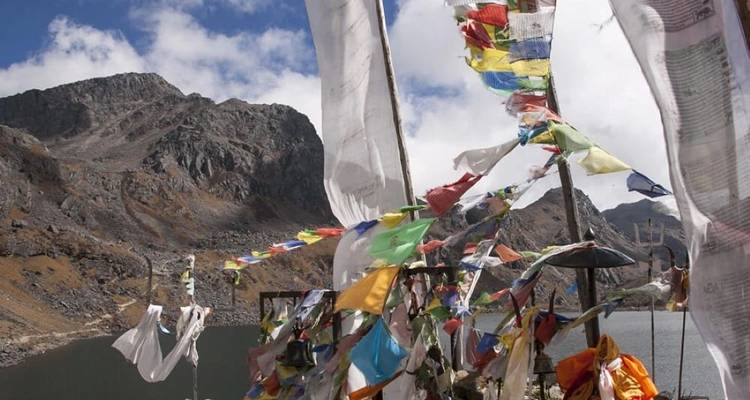 Prayer flags fluttering near a lake with rocky mountains.