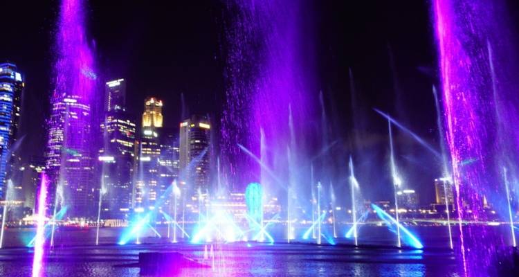 Farbintensive Brunnen- und Lasershow vor Singapurs moderner Skyline bei Nacht.
