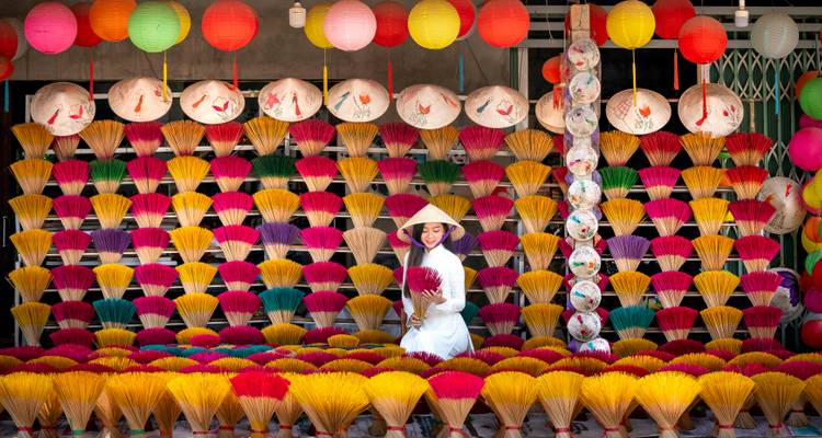 Woman with conical hat sitting among colorful incense sticks.