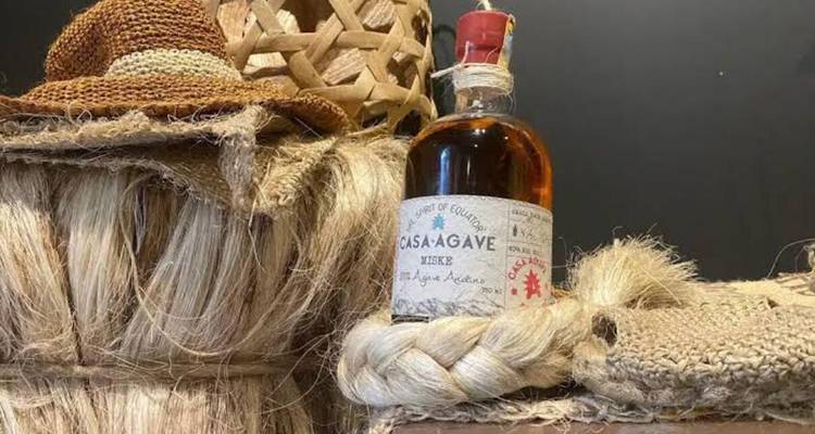 Rustic display of a mezcal bottle surrounded by coarse agave fibres and a straw hat.