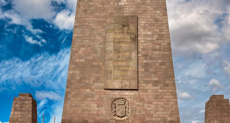 Stone monument at the Equator line rises against a vivid blue-and-white sky.