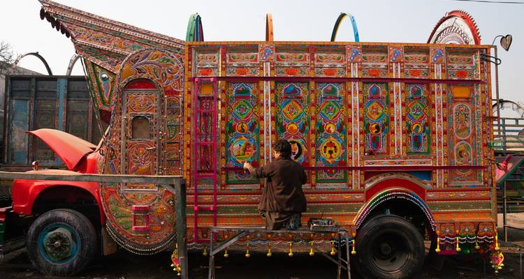 Kleurrijk versierde vrachtwagen met ingewikkelde patronen en een persoon die aan het schilderen is.