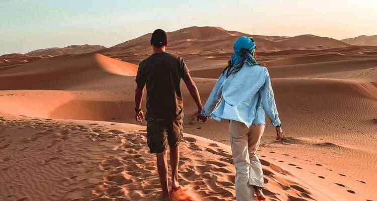 Paar geht Hand in Hand über Sanddünen bei Sonnenuntergang.