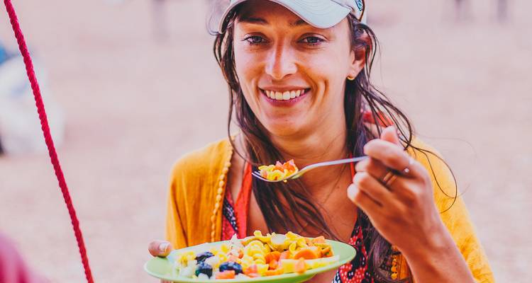 Glimlachende vrouw die een bord met kleurrijk eten vasthoudt buitenshuis.