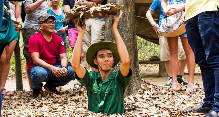Personne émergeant d'un tunnel entouré de feuilles, avec des spectateurs à proximité.