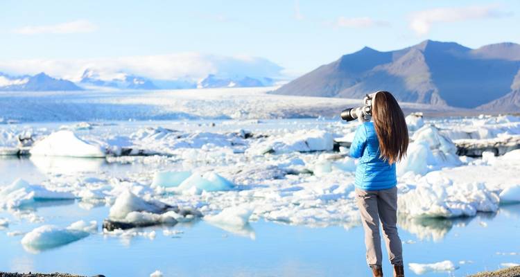 Eine Frau, die eine Gletscherlagune voller Eisberge fotografiert.