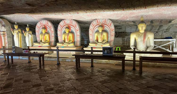 Une rangée de statues de Bouddha assis encadrées par des arches colorées à l'intérieur d'un sanctuaire de grotte faiblement éclairé.